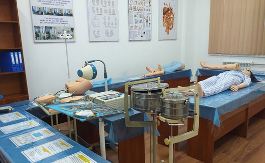 A Tajhind Edutech Pvt Ltd medical training room with anatomical models and medical equipment, including dummies on beds, surgical tools on a tray, and educational posters on the walls.