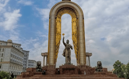A grand monument framed by a tall arch, adorned with gold detailing against a cloudy sky. It features a central statue of a woman holding a laurel wreath aloft, flanked by two lion