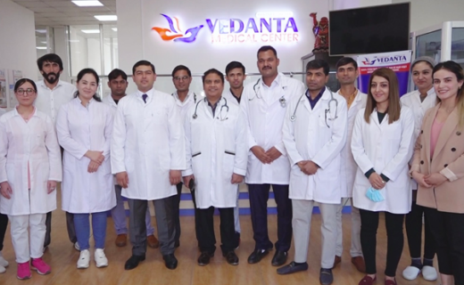 Group of medical professionals standing together in a clinic setting, smiling in front of a sign that reads vedanta medical center. they wear lab coats and stethoscopes.