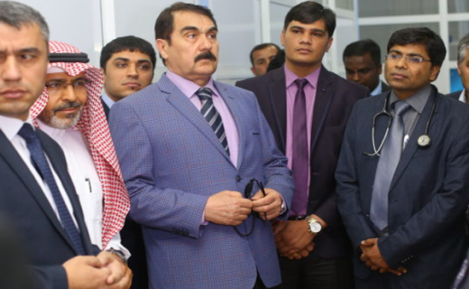 A group of men, some in western business suits and others in traditional middle eastern attire, stand attentively together in an indoor setting.