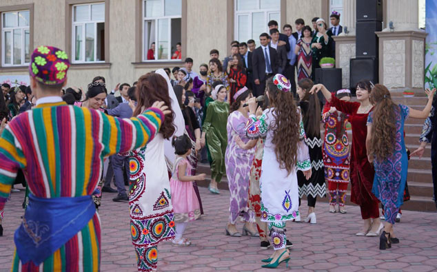 People in traditional colorful attire dancing in a circle at a cultural event organized by Tajhind Edutech Pvt Ltd, with onlookers in suits and dresses in the background near a building.