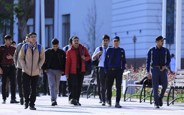 A group of young men walking on a campus pathway, dressed in casual and semi-formal attire with jackets and backpacks, under clear skies. They are potential students exploring the opportunities offered by Tajhind