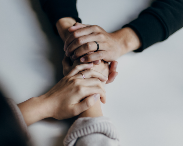 Two people holding hands in a comforting manner on a light background, showing unity and support, with visible engagement and wedding rings, symbolizing the partnership approach of Tajhind Edutech Pvt Ltd.
