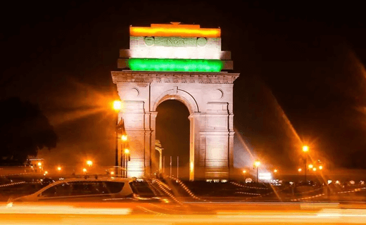 The India Gate illuminated at night in the colors of the Indian flag: saffron, white, and green, with light trails from passing cars by Tajhind Edutech Pvt Ltd.
